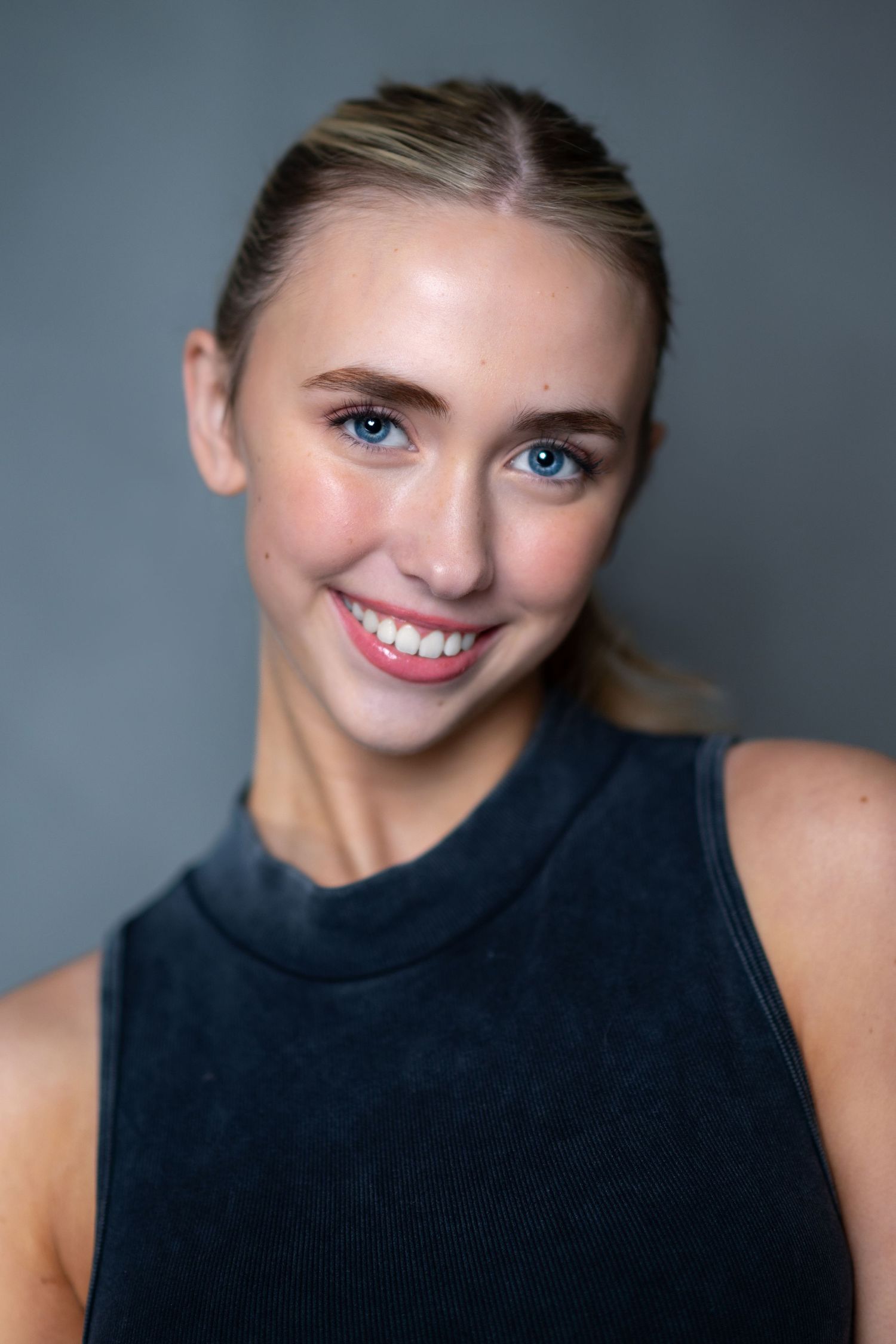 Portrait of someone wearing a black sleeveless top while smiling against a grey backdrop.