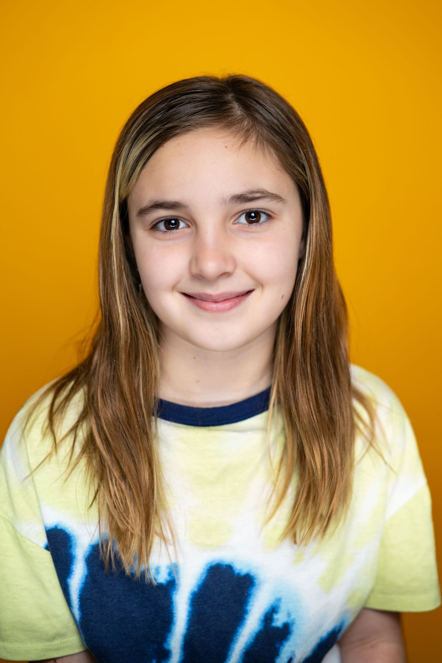 Casual studio portrait with yellow backdrop features gentle smile and tie-dye shirt.