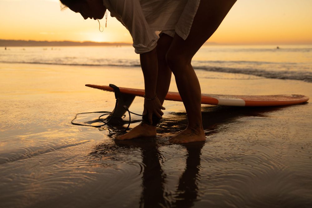 woman tying board leash to ankle on Maui beach