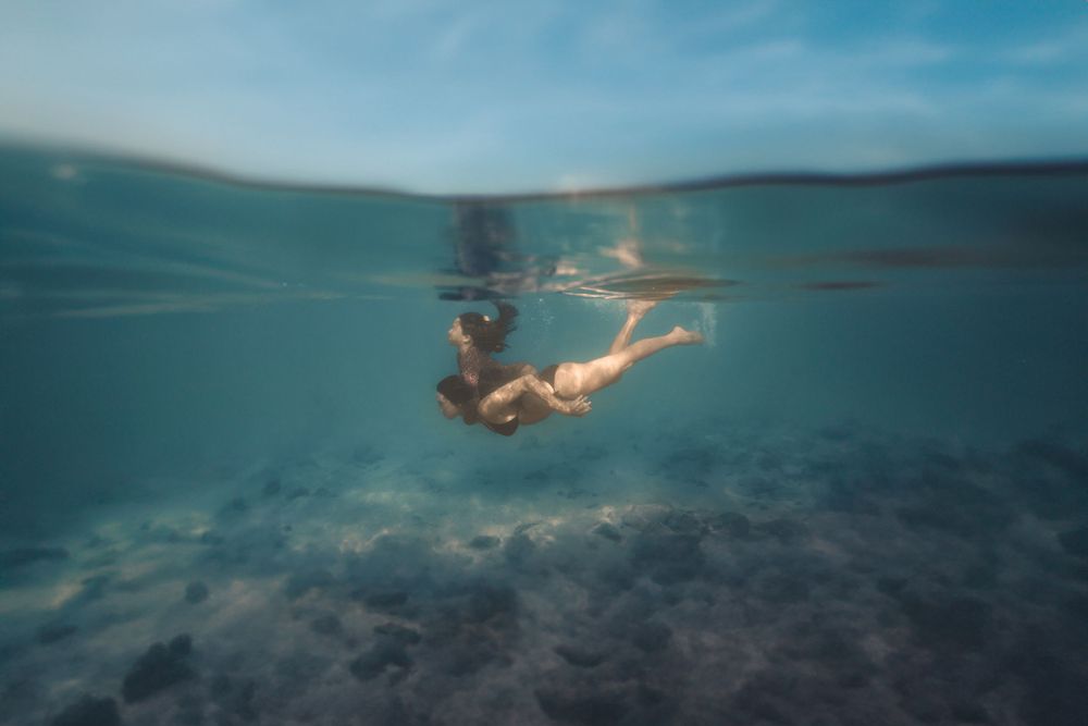 mother swimming underwater with daughter on back on Maui