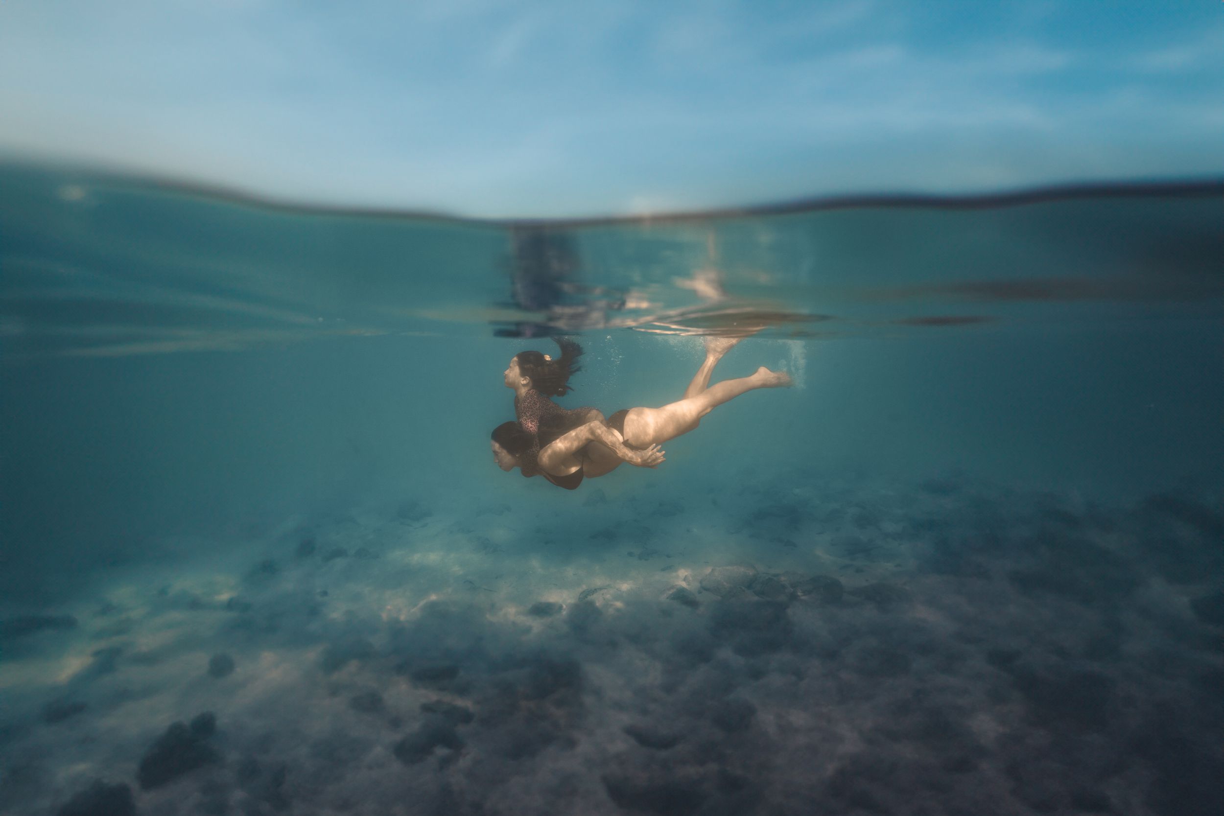 mother swimming underwater with daughter on back on Maui