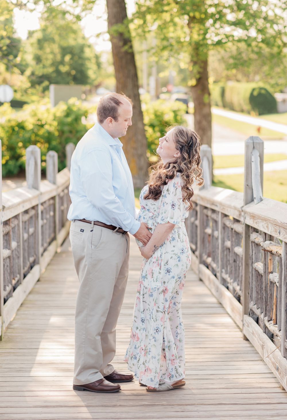 Expecting mother standing on a bridge over looking a lake with her husband looking into each other's eyes.
