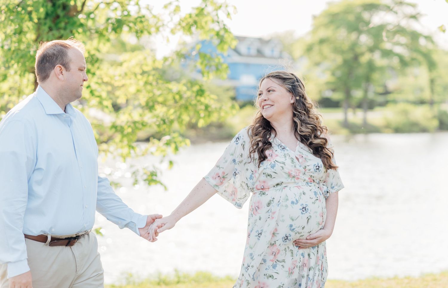 Expecting wife looking back at her husband while holding hands in front of a lake.