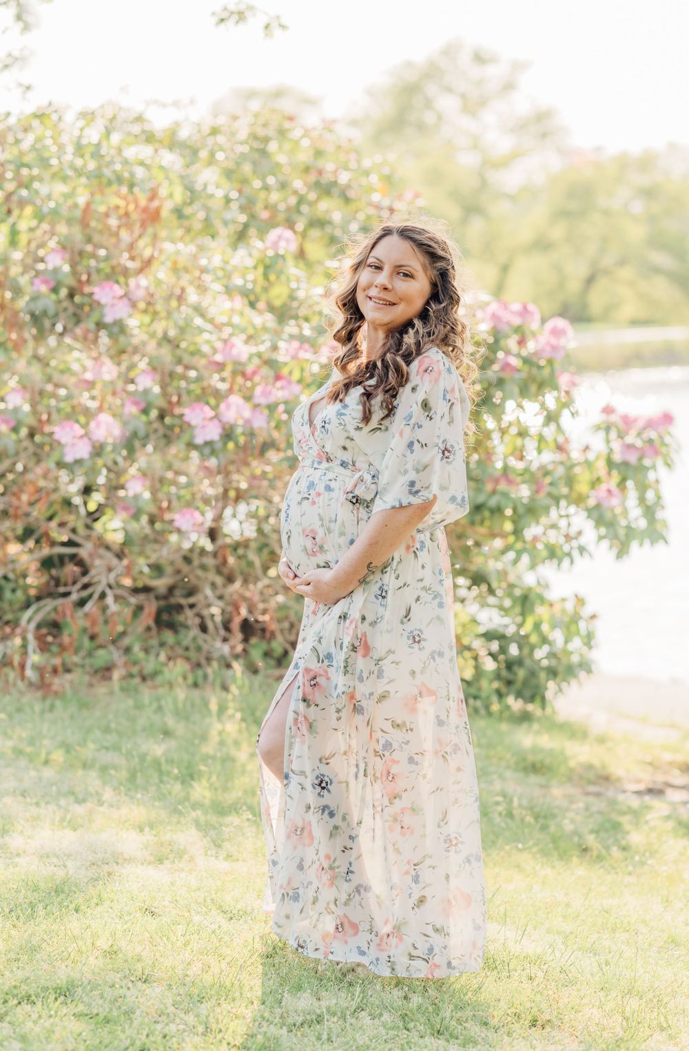 Portrait of a pregnant woman in a park wearing a floral dress, smiling.