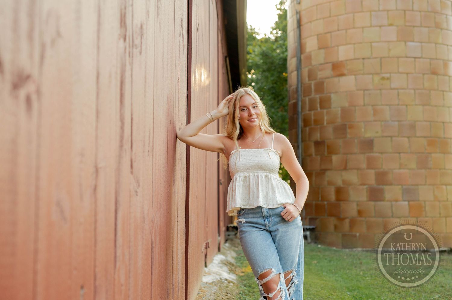 Rustic outdoor portrait against a red barn wall wearing casual denim and white top in warm sunlight.