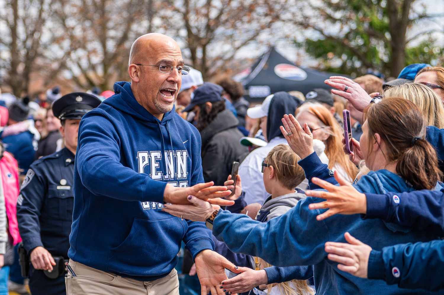 Person in Penn sweatshirt enthusiastically high-fives fans in crowd during outdoor sporting event.