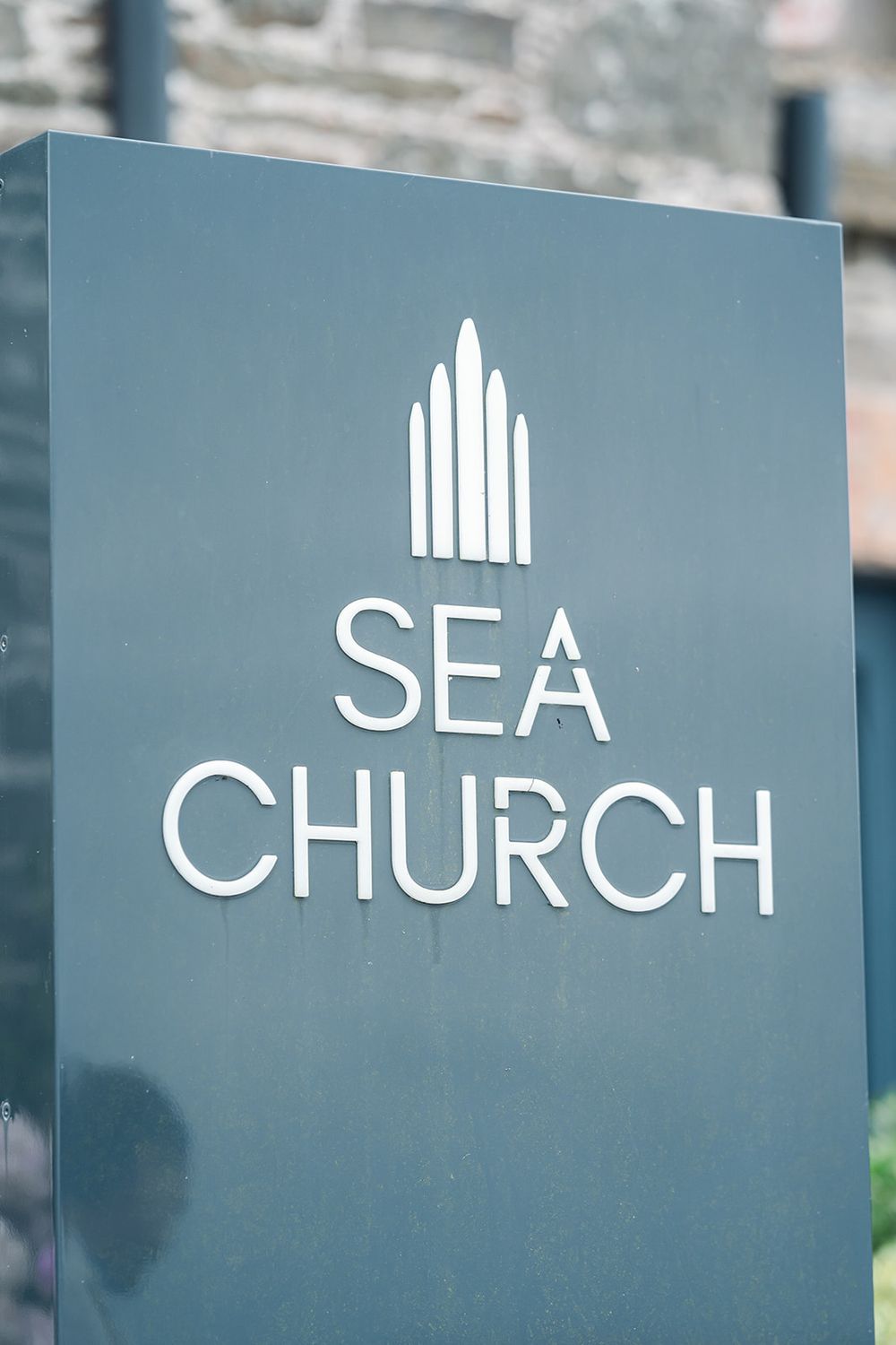 A modern grey sign for Sea Church featuring a minimalist steeple design.