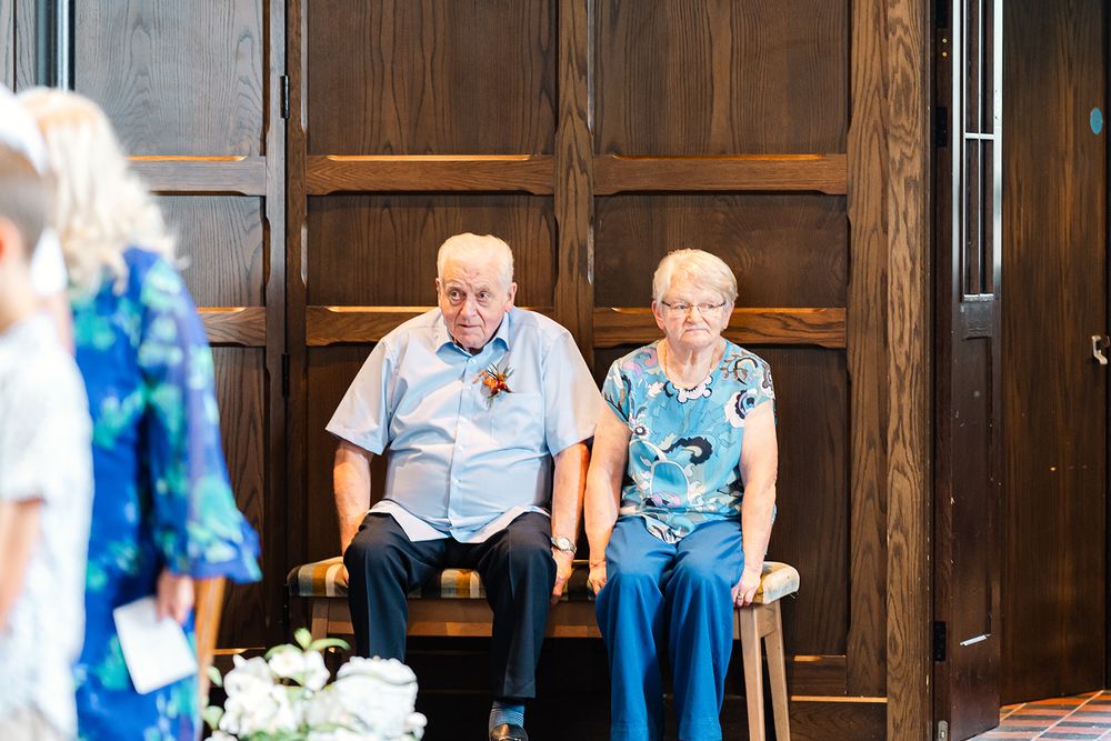 Wedding guests seated on wooden chairs during ceremony in historic venue.