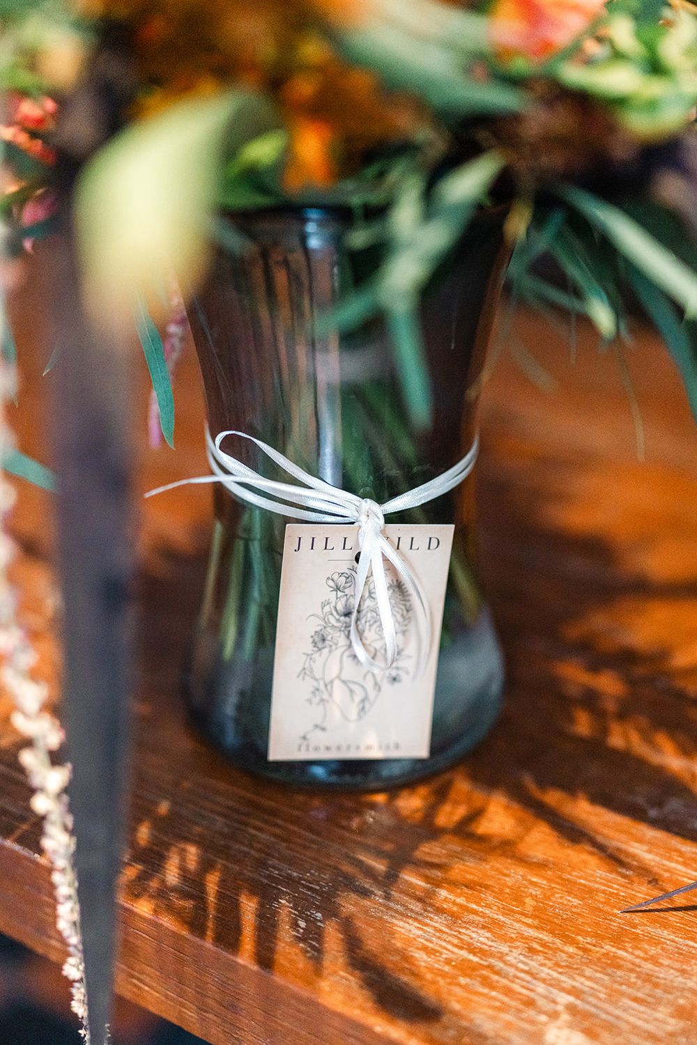 A decorative tag tied with white ribbon to a dark vase on a wooden surface.