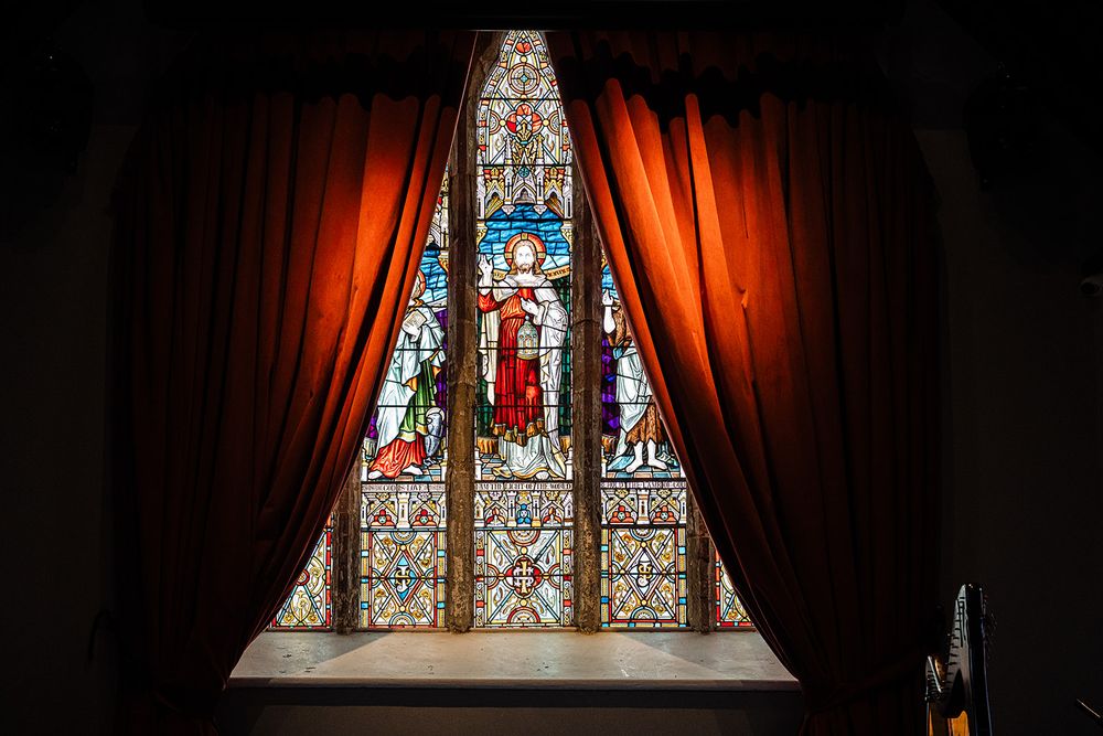 A dramatic stained glass church window framed by red curtains.