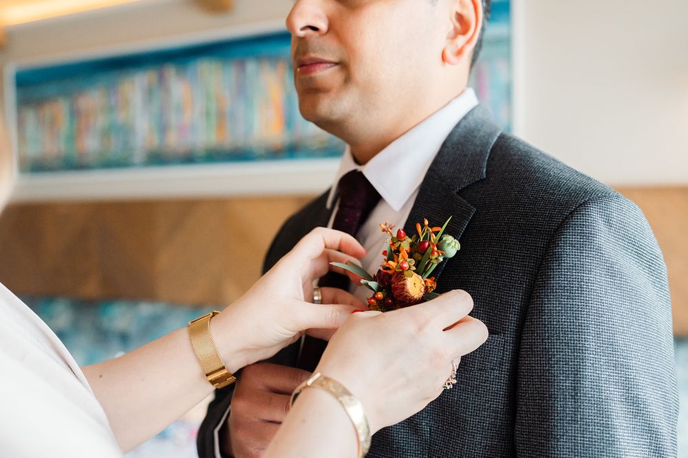 A boutonniere being pinned to a grey suit jacket.