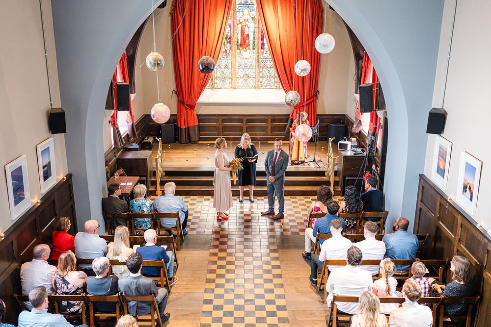 View of an indoor wedding ceremony with orange curtains and checkered floor in an intimate venue.