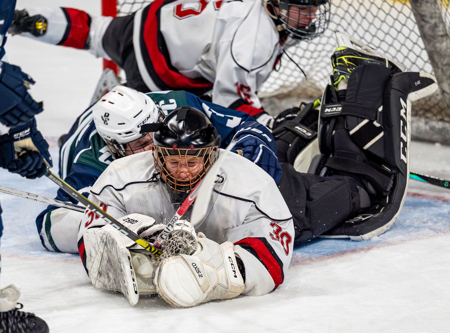 Hockey goalie makes sprawling save on ice during intense game action.