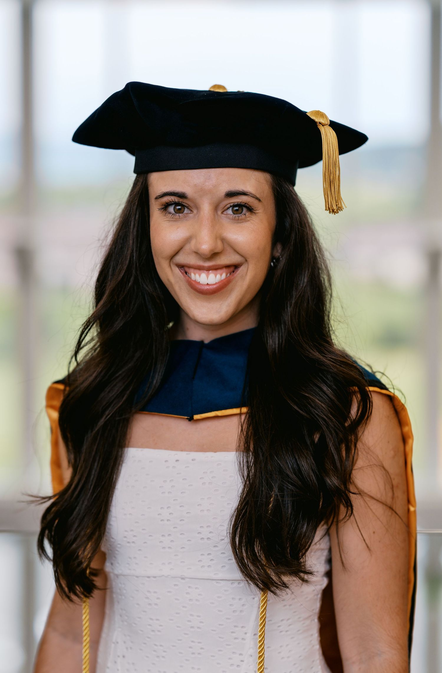 Graduate wearing traditional commencement regalia with black mortarboard cap and yellow tassel smiles in portrait photo.