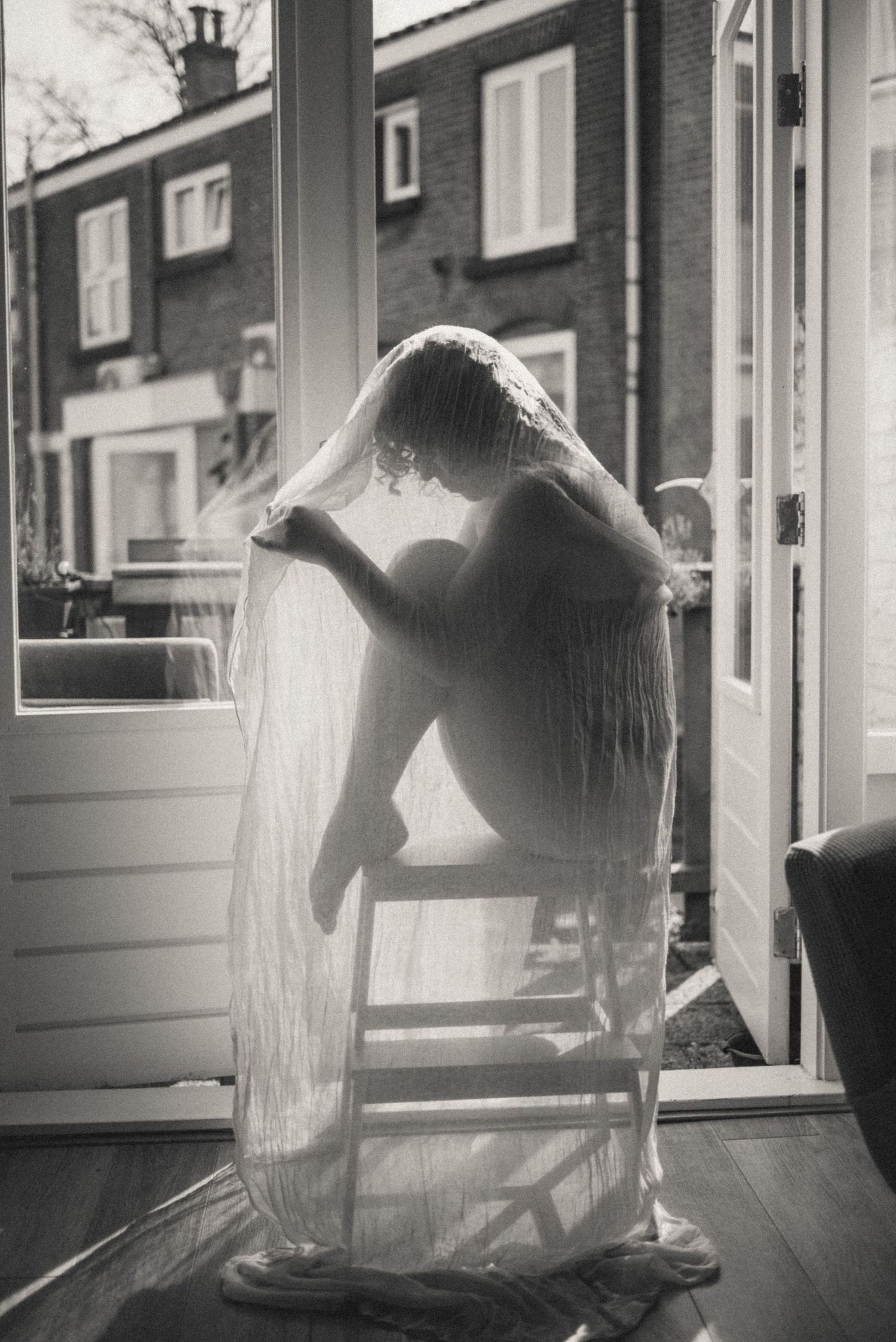 Cozy at-home boudoir photoshoot: black and white cinematic candid photo of a woman sitting on a chair in lingerie. Natural and intimate mood