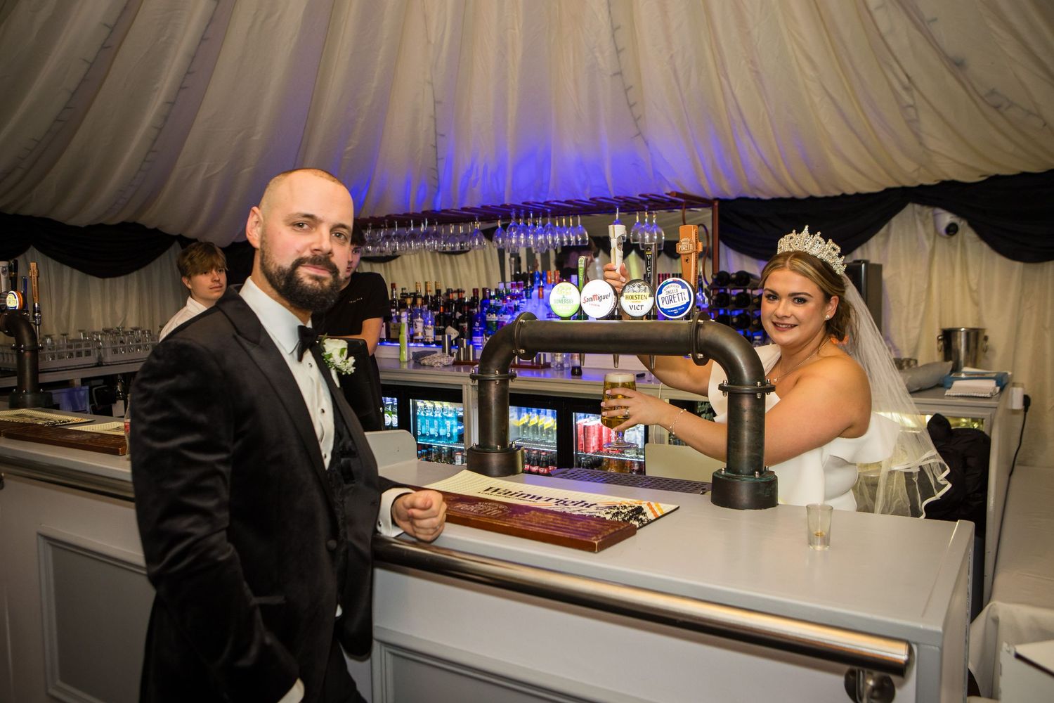 A playful wedding moment at an illuminated bar with blue lighting.