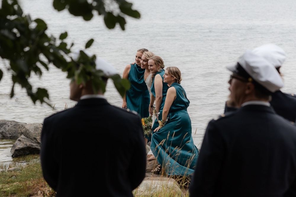 Wedding party wearing teal dresses gather near a waterfront during an outdoor celebration.