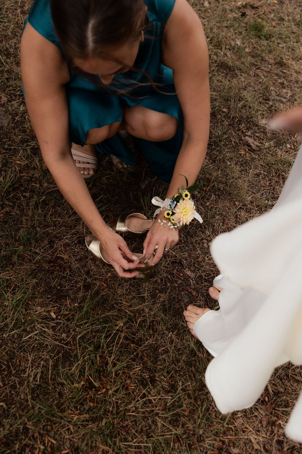Person in a teal dress planting something in brown soil as someone in white stands nearby watching.
