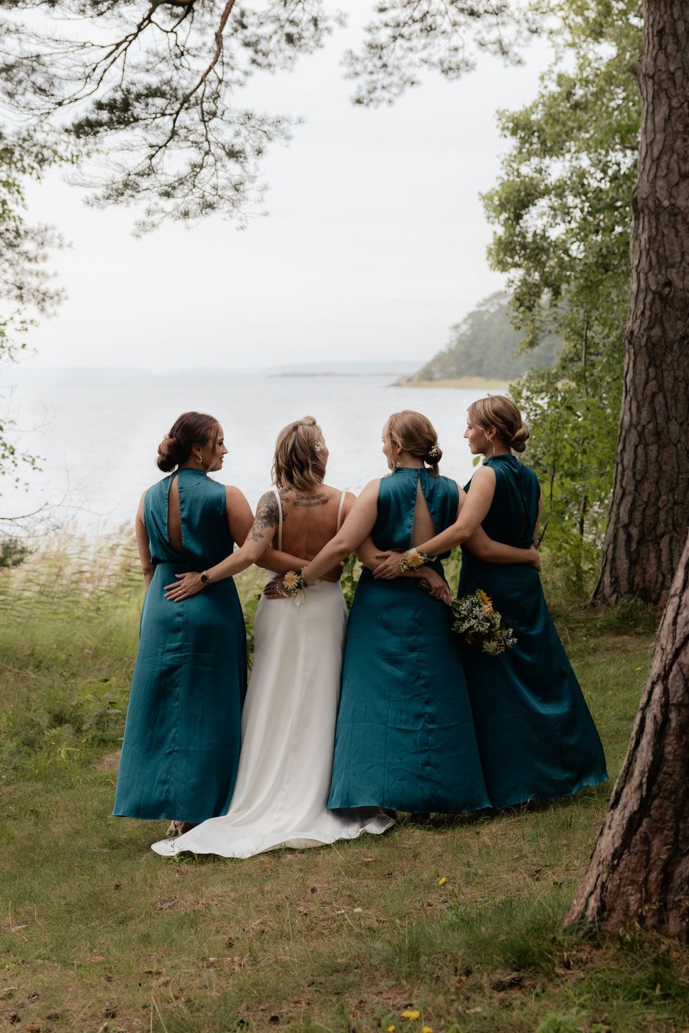 Wedding party in teal bridesmaid dresses stand with bride in white gown at coastal overlook location.
