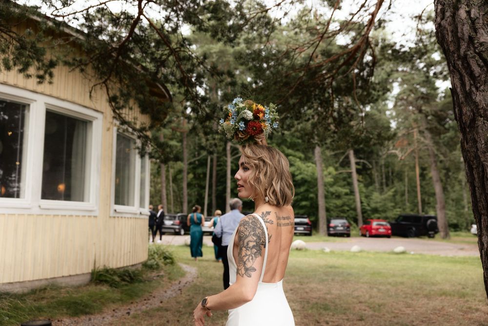 A minimalist outdoor wedding scene with a white gown and floral crown amidst pine trees and a rustic backdrop.