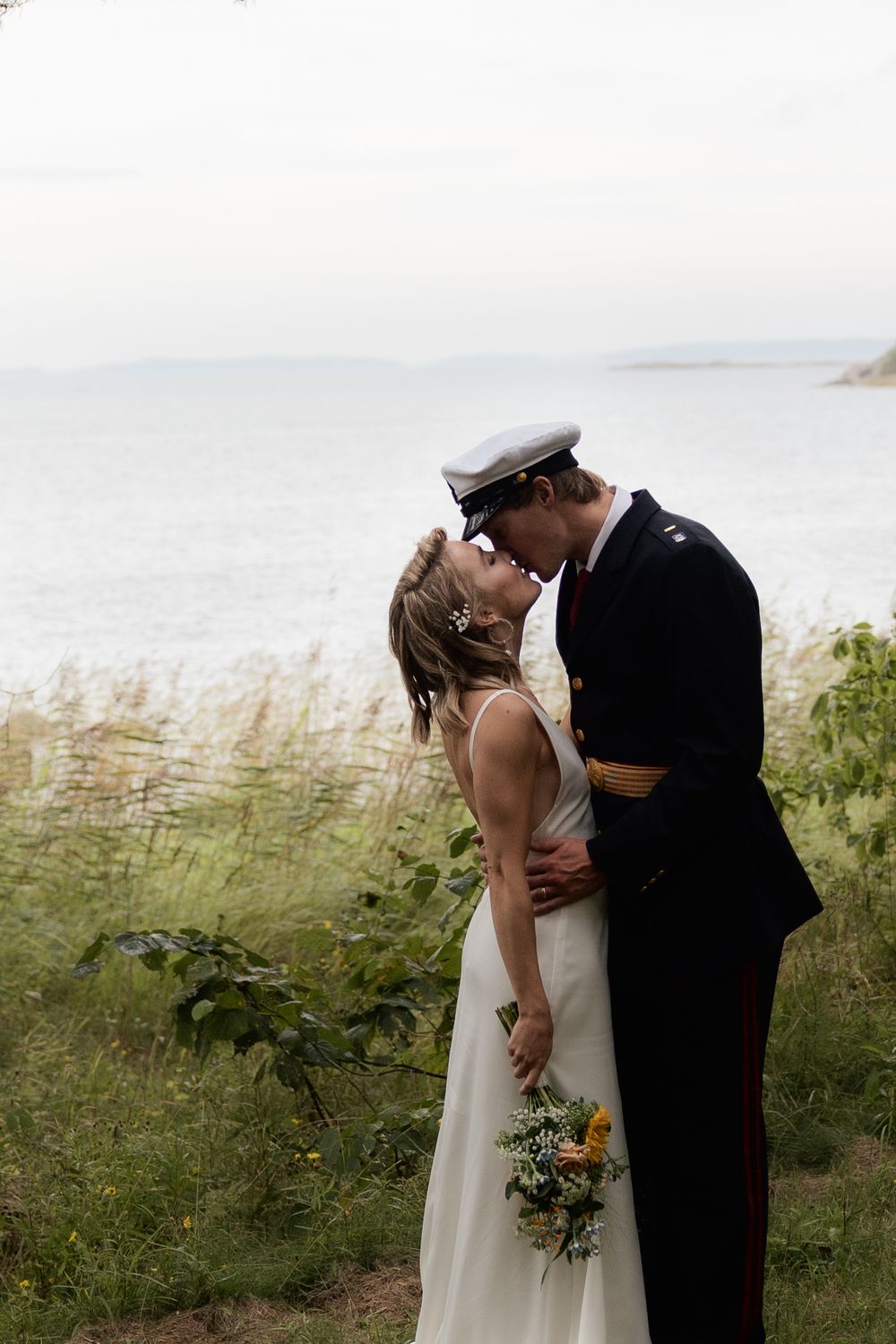 A romantic seaside wedding couple sharing an intimate moment against a misty coastal backdrop with tall grass.