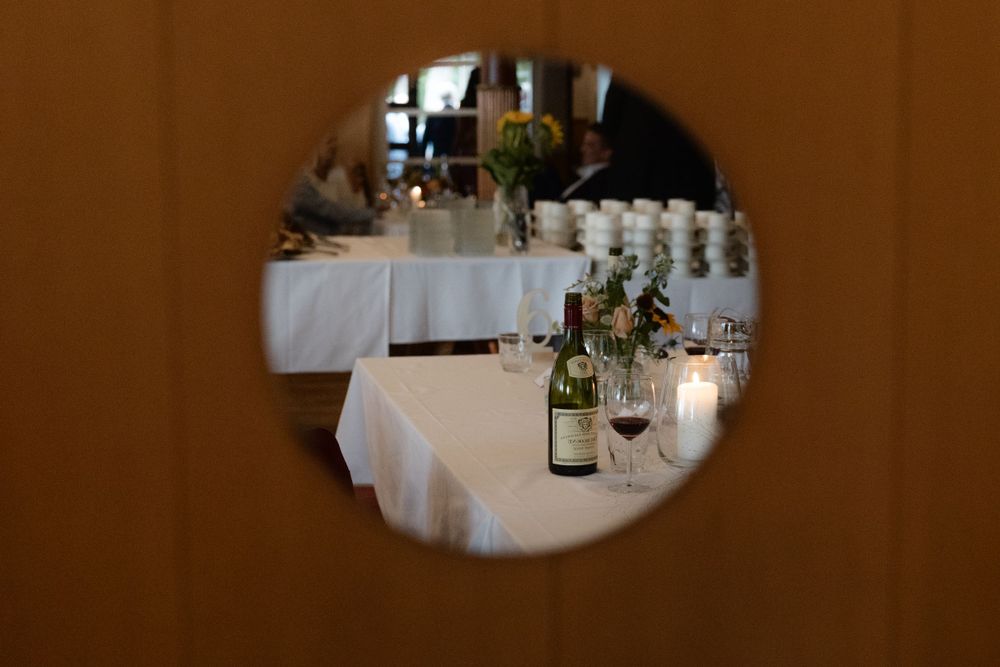 White tablecloths and wine bottles set up for an elegant dining event viewed through a circular opening.