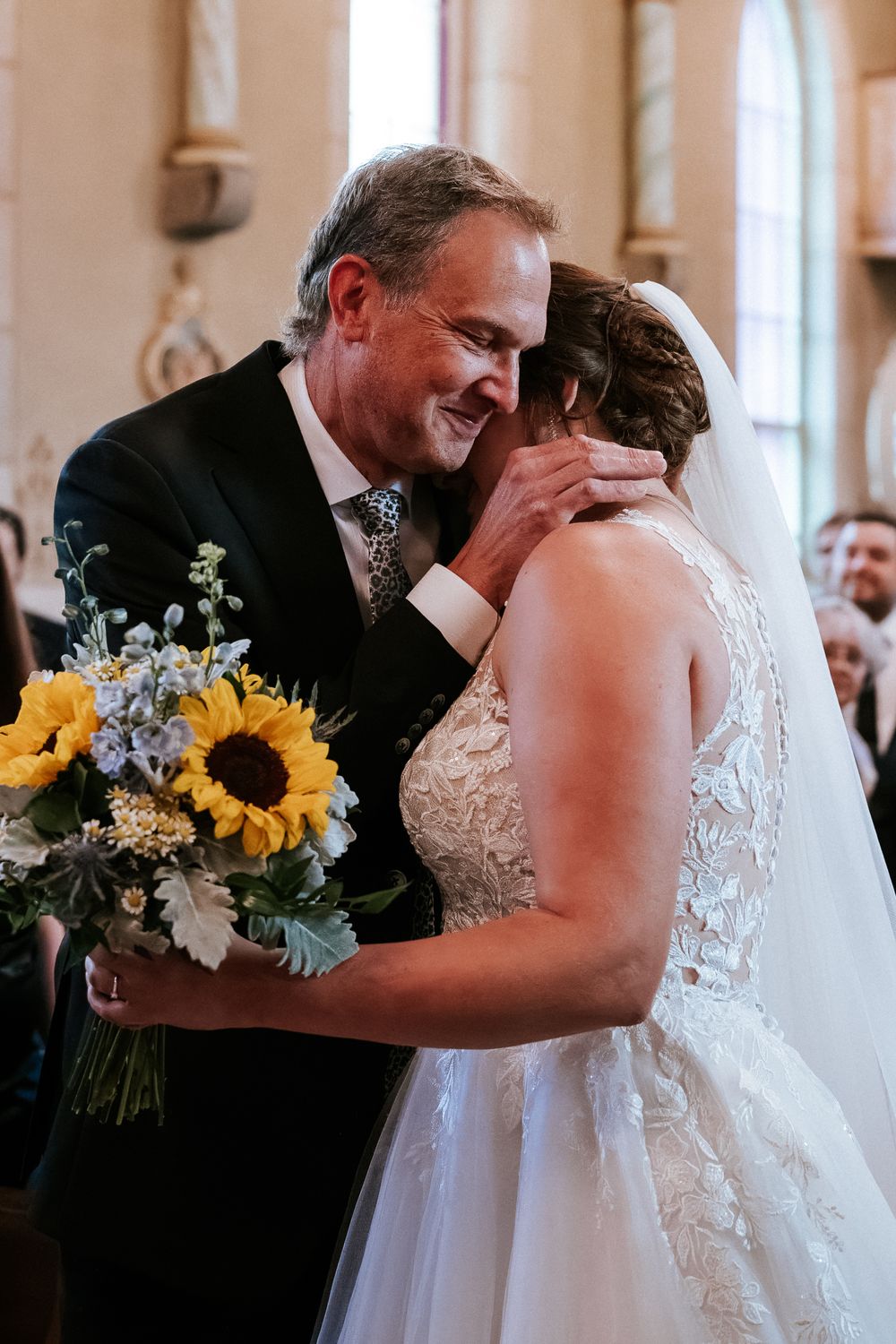 Un moment joyeux de mariage avec des tournesols et des détails délicats en dentelle dans un cadre d'église élégant.