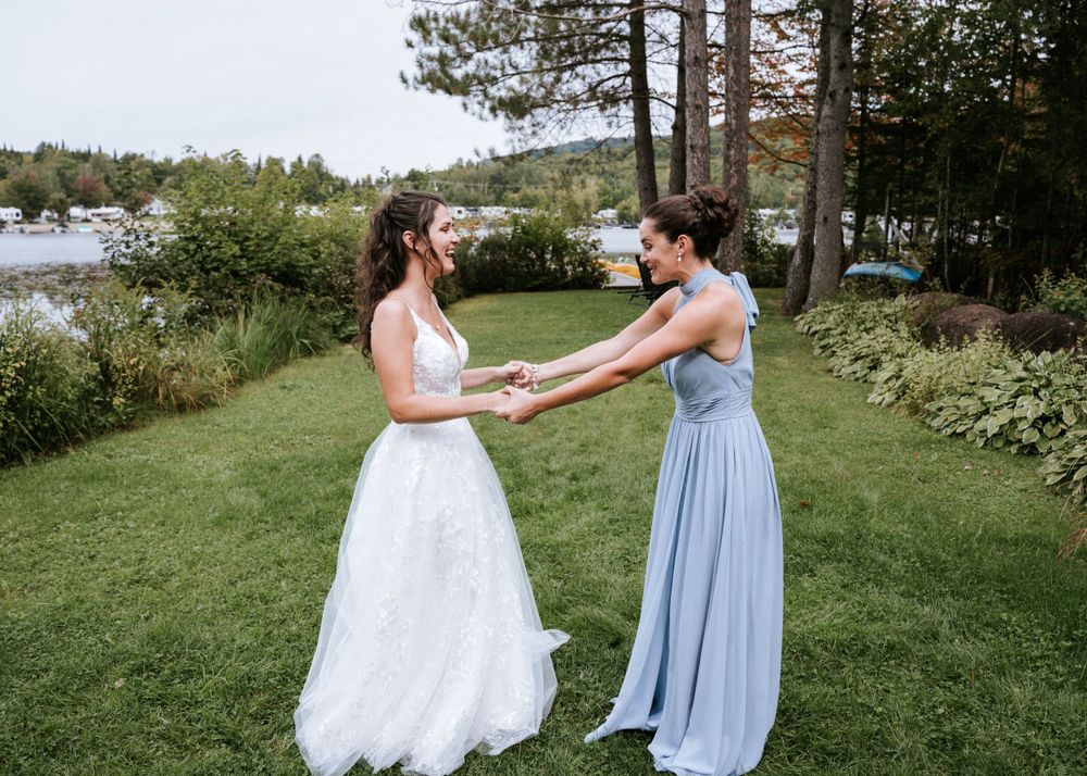 Deux personnes en robes de soirée partagent un moment joyeux sur une pelouse au bord du lac, entourées d'arbres et de jardins.