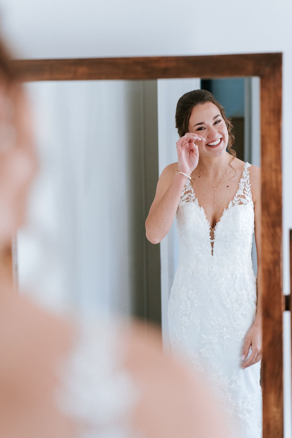 Une mariée en robe de dentelle blanche sourit joyeusement pendant ses préparatifs dans une pièce aux accents de bois.