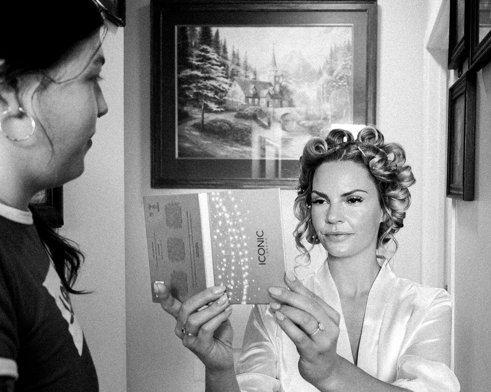 Black and white photo of bride looking into a compact mirror while getting ready