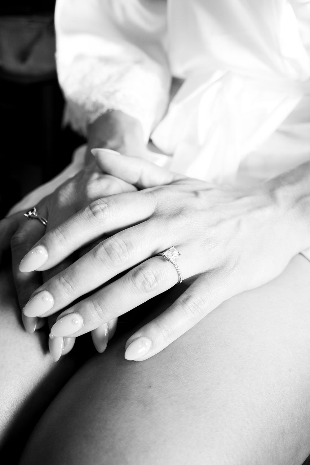 Black and white close-up of hands with rings resting on a smooth surface in an artistic composition.