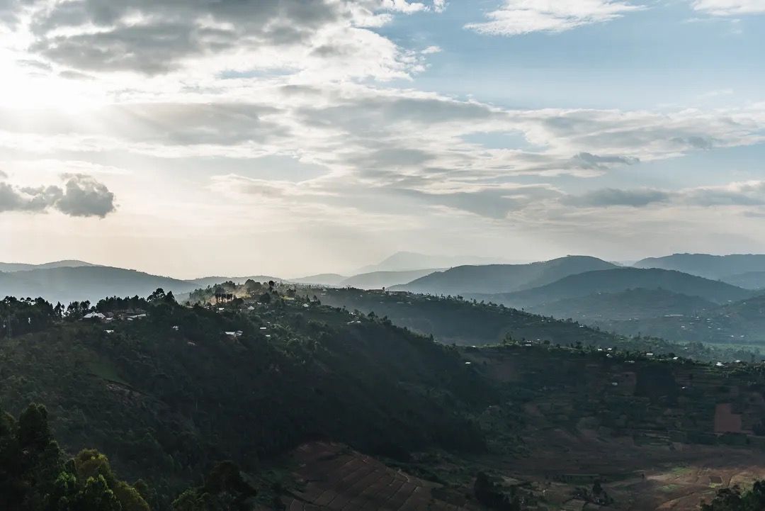 Sunlight breaks through clouds over layered hills, highlighting dramatic skies, depth and scenic mountain views.