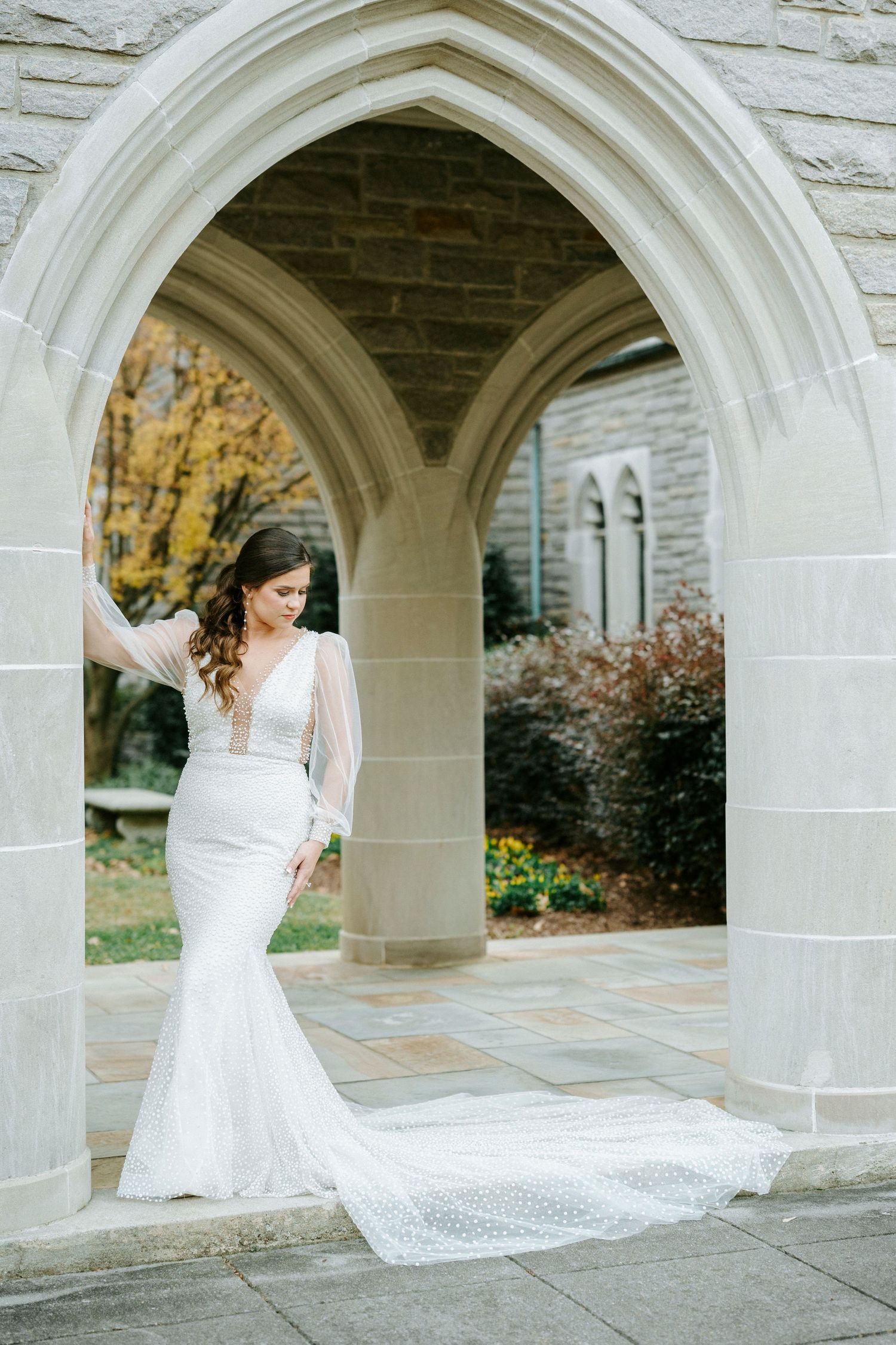 An elegant bridal portrait showcasing a fitted lace wedding dress with a flowing train under stone arches.