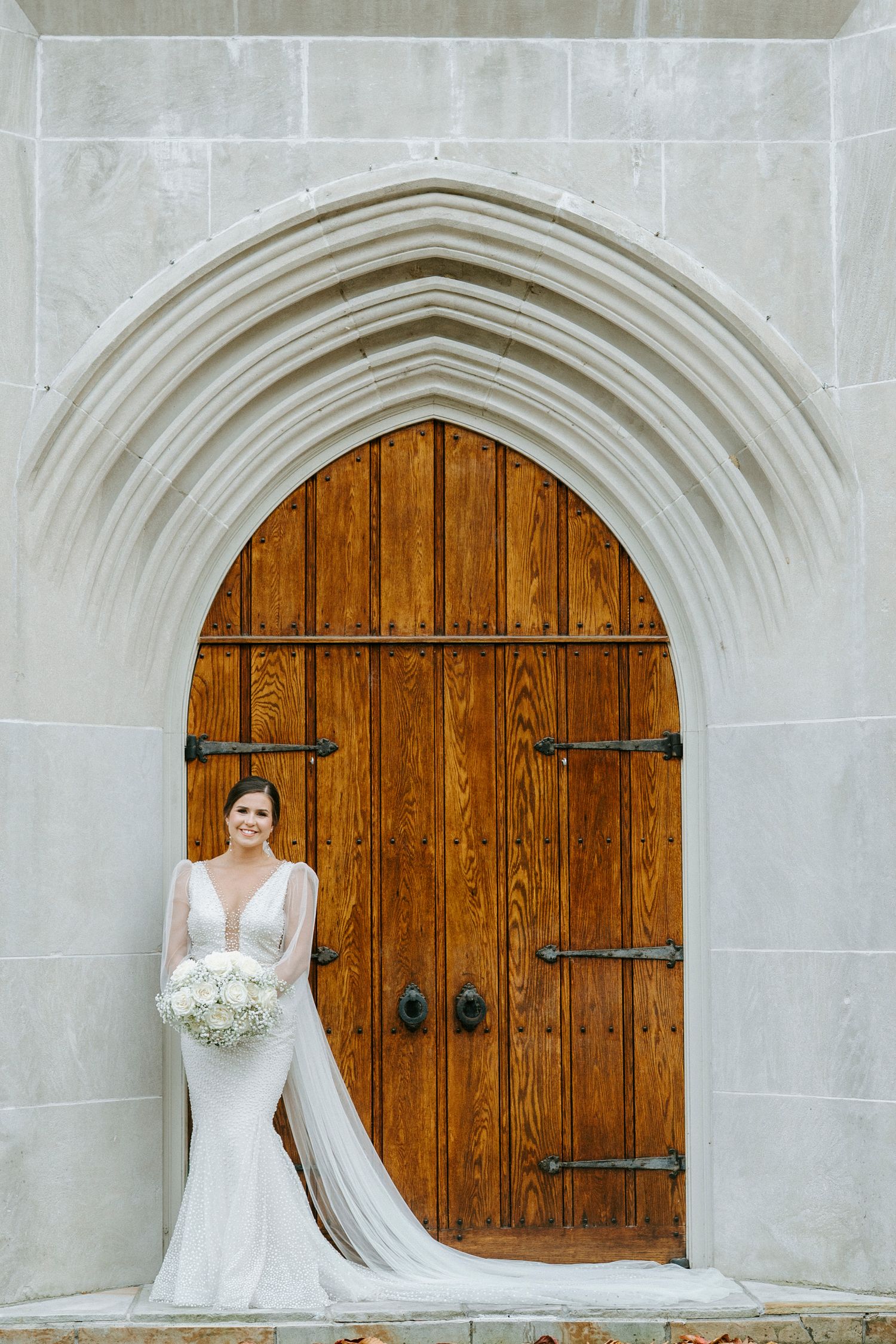 An elegant bridal portrait against a wooden church door framed by a gothic stone archway.