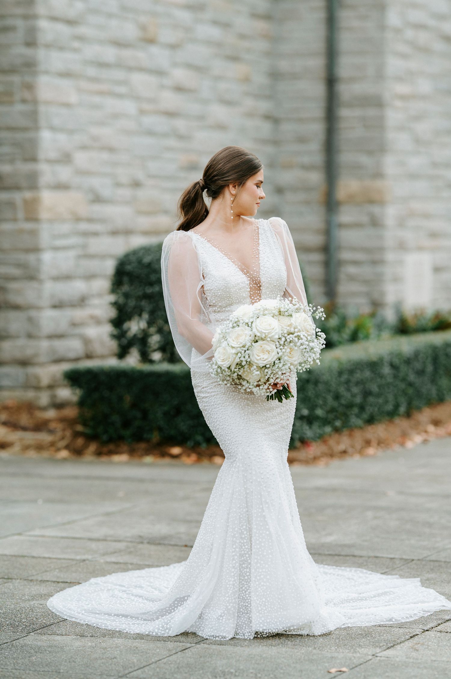 Elegant mermaid wedding dress with sheer long sleeves and deep v-neckline paired with white floral bouquet.