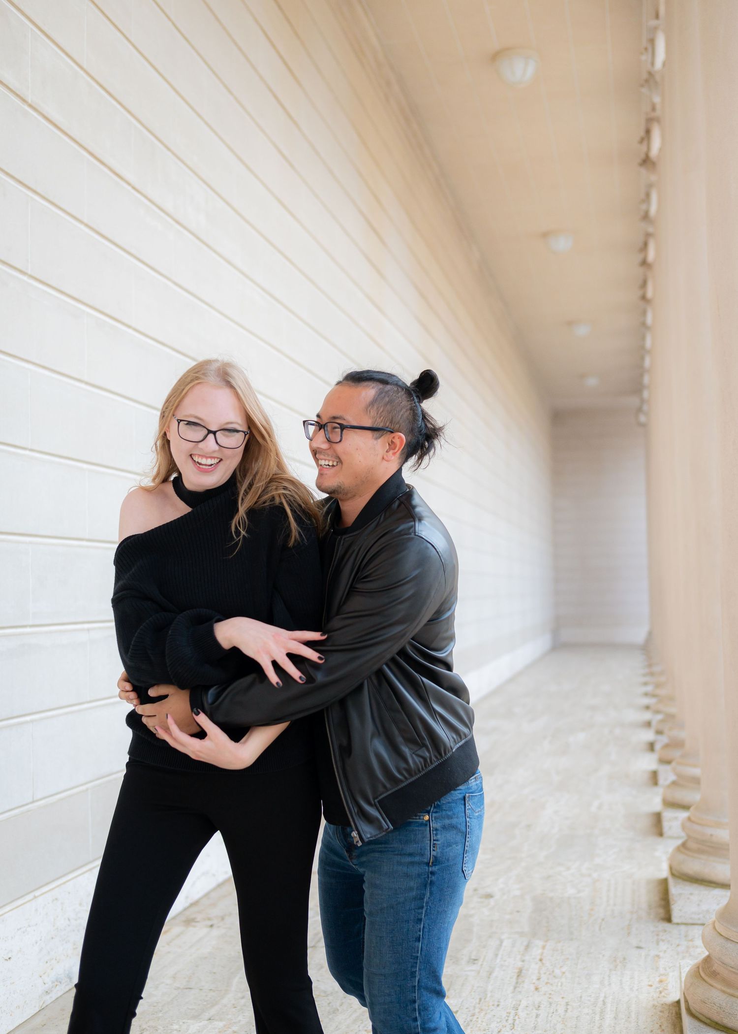 A couple sharing a playful moment in a white hallway with track lighting.