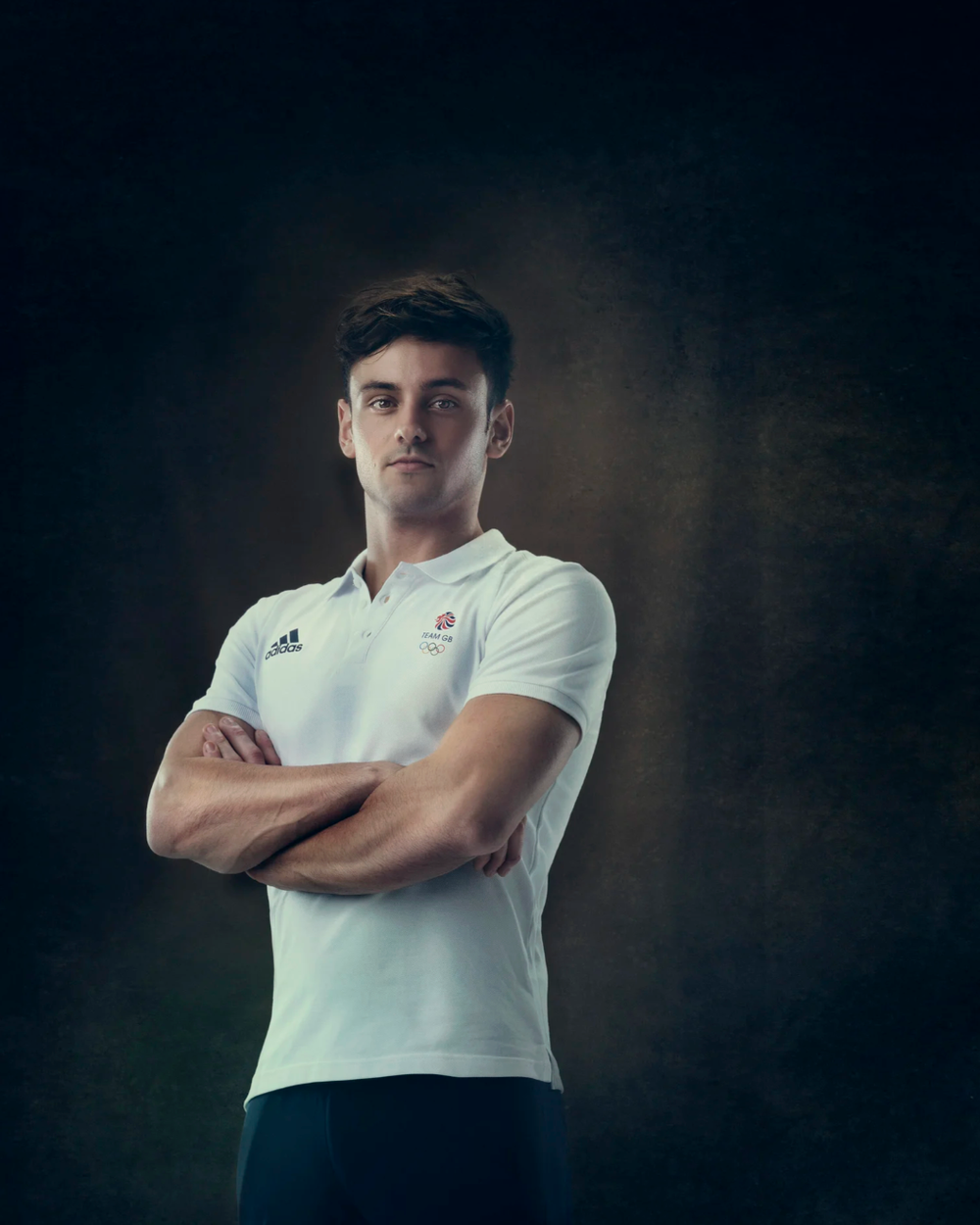 Professional portrait against dark background showing person in white polo shirt with crossed arms.