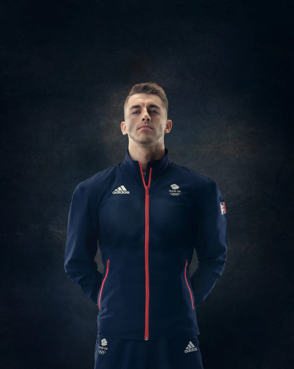 Sports figures in dark navy jackets photographed against moody black background.