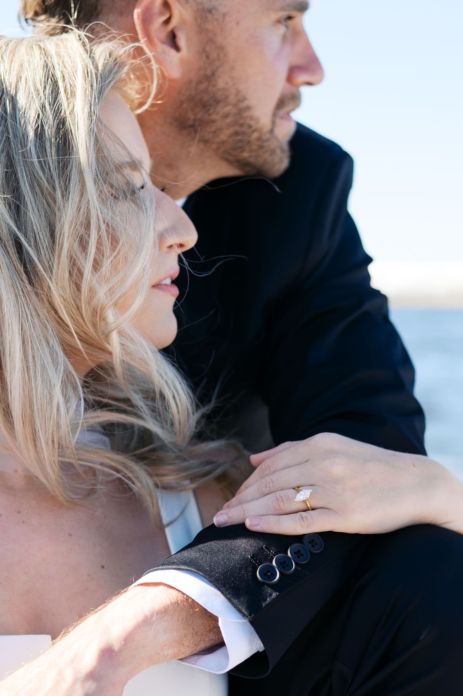 A couple shares an intimate moment by the ocean with a focus on their hands and profiles in black and white tones.