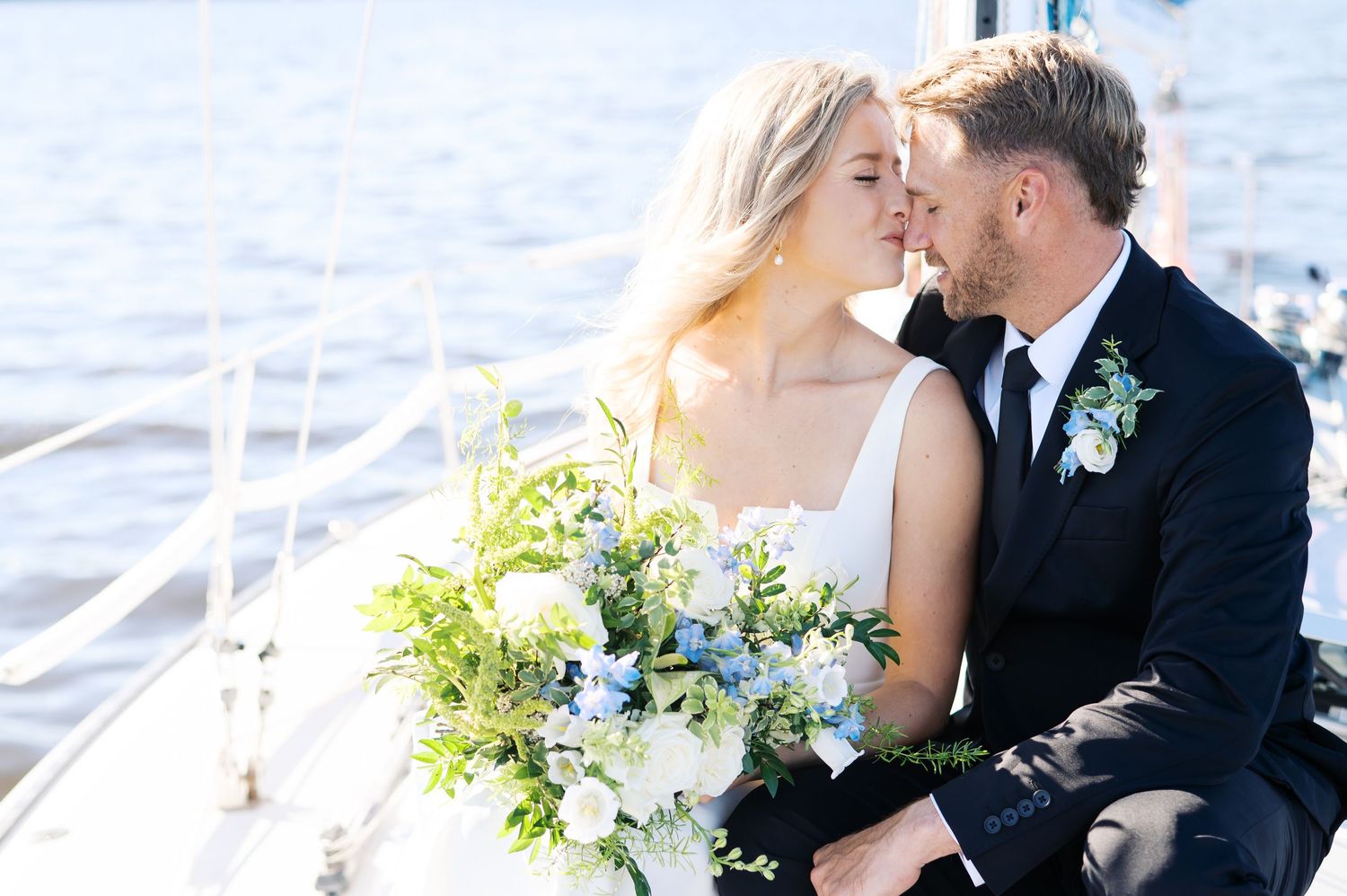 Newlyweds share an intimate moment on a sunny day with a beautiful white and green floral bouquet. Sailboat elopement photography