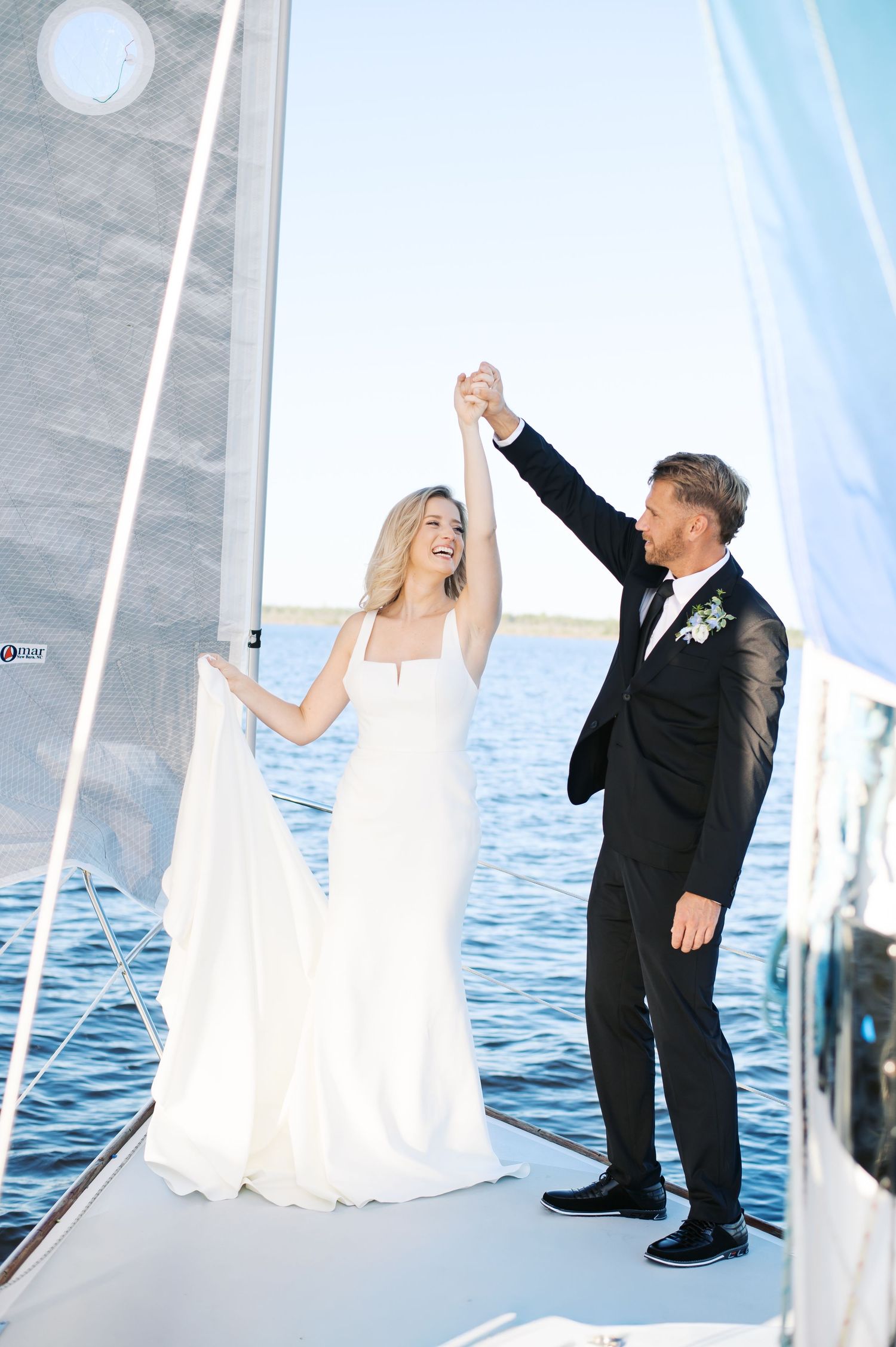 Wedding couple dancing and twirling on a boat deck with white sails and ocean views. Photo by Heather Moss Photo