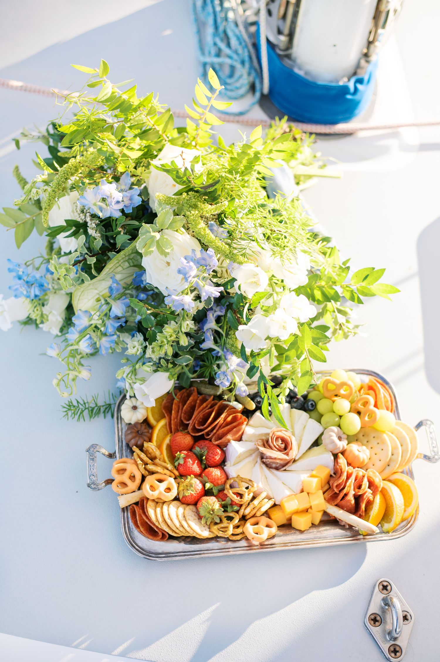 Elegant wedding reception charcuterie board with fresh flowers, cheese, fruits and appetizers on a white surface. Coastal wedding inspo.