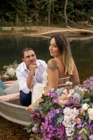 Elegant boat photoshoot with lush floral arrangements in purple and white on calm waters.