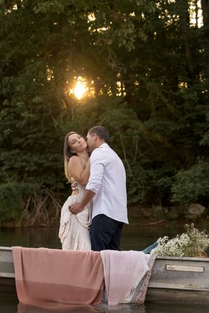 A couple sharing an intimate moment on a boat during golden hour near a wooded shore.