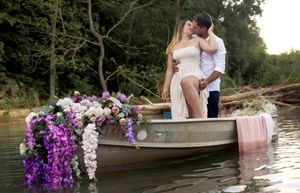 Couple sharing a romantic moment on a boat adorned with purple and pink floral arrangements.