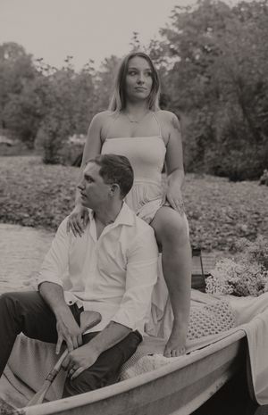 Vintage style portrait of a couple posing in a wooden boat by the riverbank.