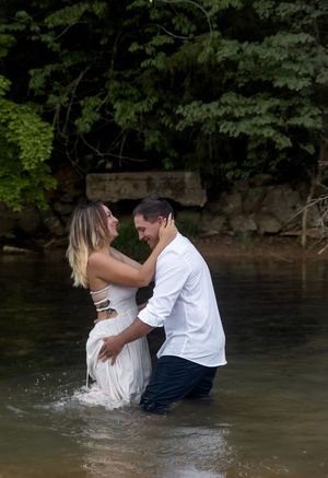 Playful couple splashes in lake water during romantic shoot.