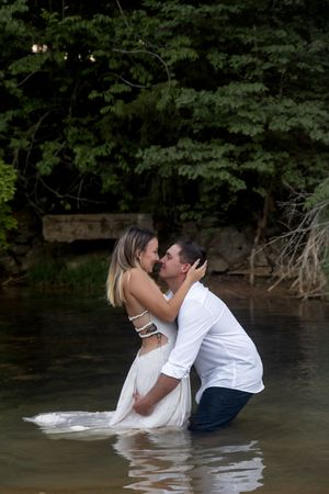 Romantic couple embraces while standing waist-deep in lake water.