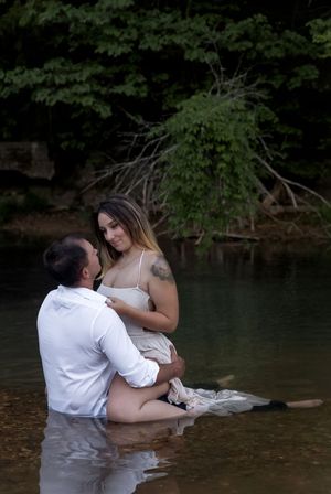 A romantic couple shares an intimate moment while sitting in shallow water surrounded by trees.