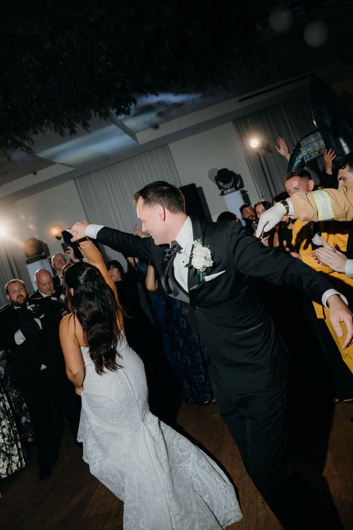 Wedding guests dance energetically on a dark dance floor during a reception celebration.